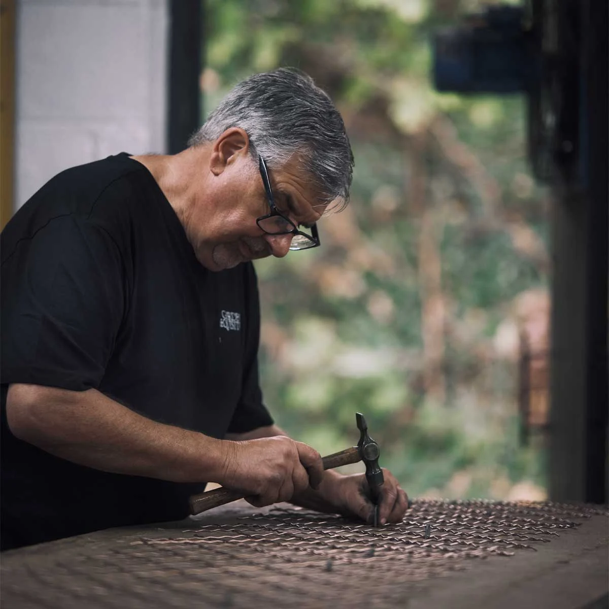 copper-wirework-pinning-01 A craftsman in the workshop is pinning crimped copper wirework into position on a baseboard ready for welding
