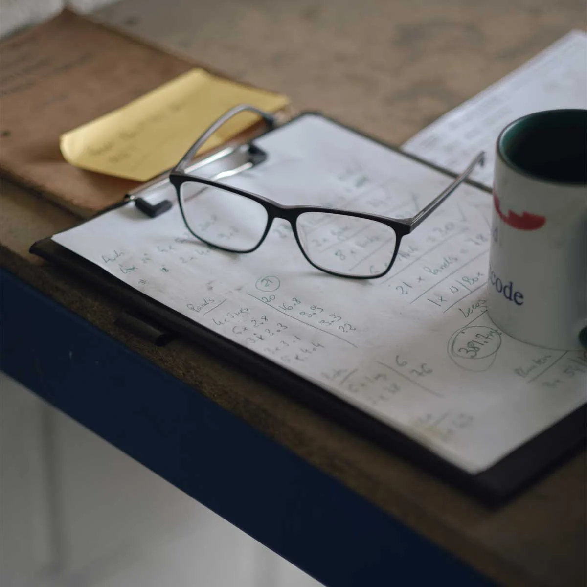glasses-and-design-notes A pair of glasses and cup of tea rest next to a page of hand written production notes on a bench in the workshop.
