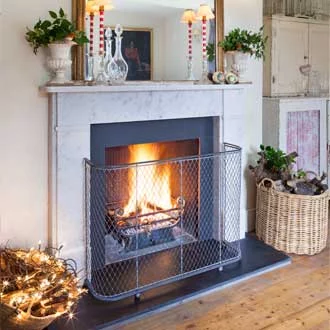 A traditional woven wirework metal fireguard around an open fireplace