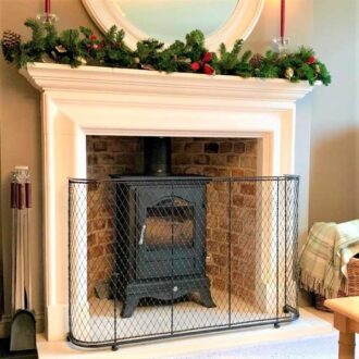 A festive decorated fireplace with log burner and a wire work fireguard