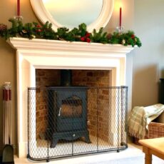 Traditional woven wire mesh fireguard in metal around a fireplace with wood burning stove