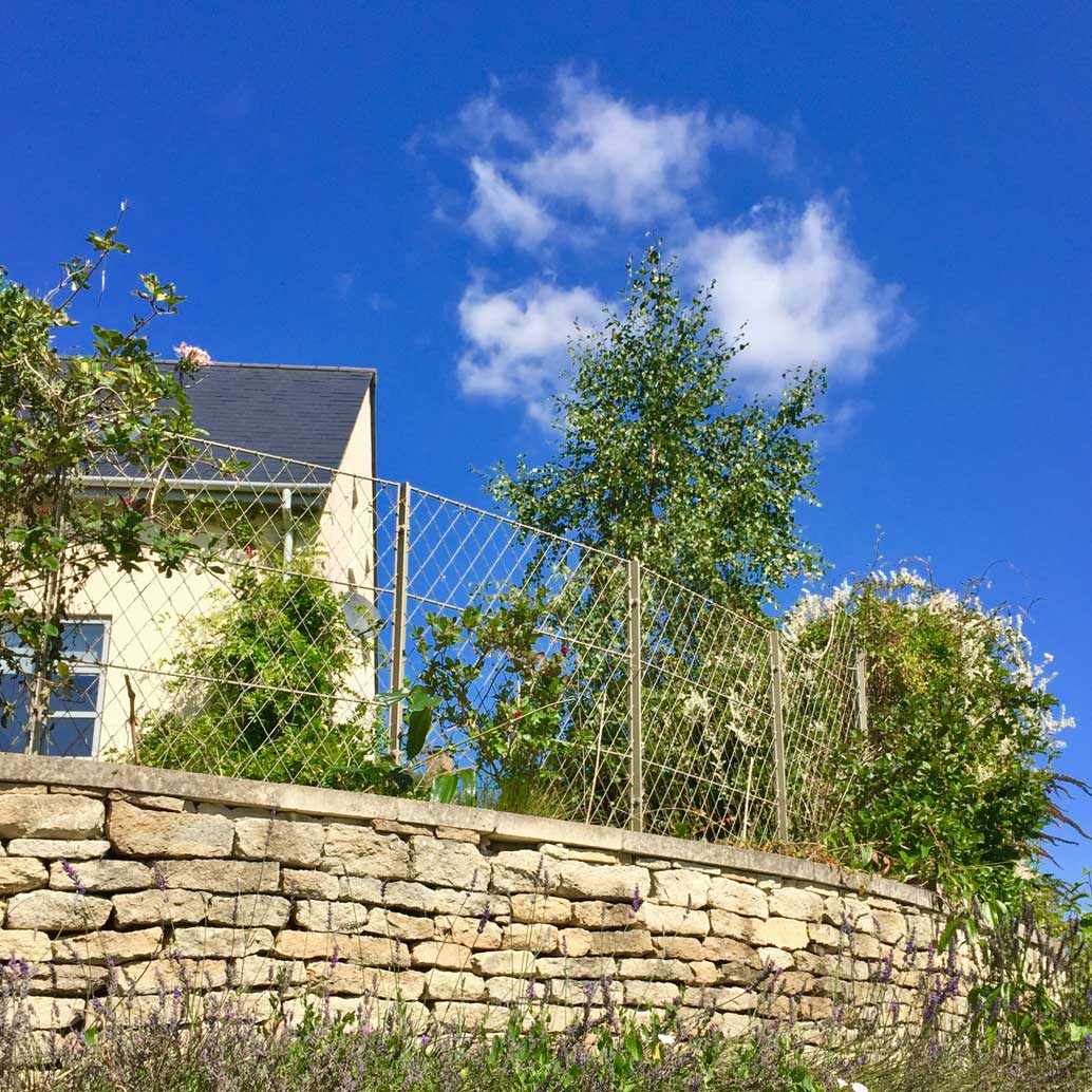 View of a dry stone wall topped with decorative woven wirework trellis panels