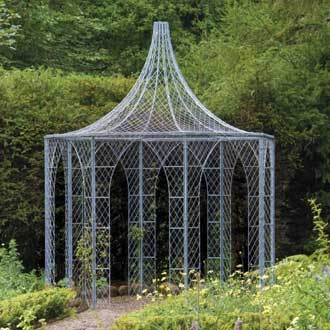 A view across a formal garden looking towards a large octagonal English wire work gazebo with dramatic roof ornamentation