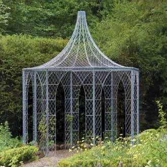 A view across a formal garden looking towards a large octagonal English wire work gazebo with dramatic roof ornamentation