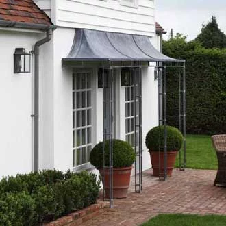 A large galvanized zinc metal porch with supporting columns at the rear of a house above patio doors.